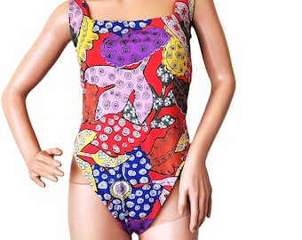 May include: A colorful one-piece swimsuit with a square neckline and thick straps. The swimsuit features a vibrant pattern of red, blue, yellow, purple, and white abstract shapes. The swimsuit is made of a stretchy material.
