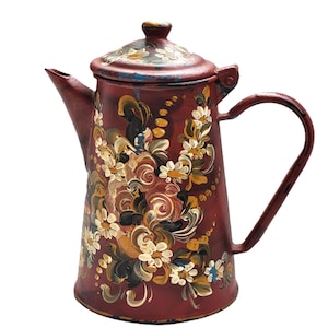 May include: A red metal teapot with a floral design painted on the side. The teapot has a lid and a handle.