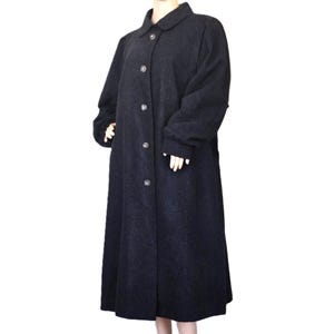 May include: A dark gray, full-length coat with a classic design. The coat features a round collar, button-down front, and long sleeves. The coat is displayed on a mannequin. The fabric appears to be a wool blend.