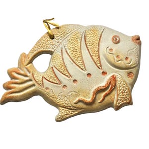Op de afbeelding: Een keramiek vis ornament met een gele en witte glazuur. De vis heeft een gedetailleerd ontwerp en een gat om op te hangen.