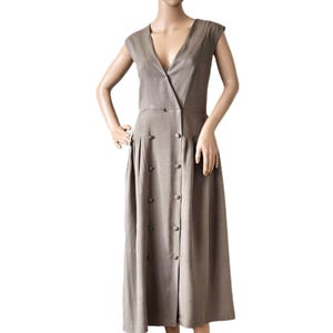 Peut inclure: Robe taupe avec un décolleté en V et des manches courtes. La robe présente un devant boutonné et une jupe midi. La robe est présentée sur un mannequin.