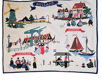 May include: A colorful needlepoint tapestry depicting scenes from Holland, including windmills, houses, and people in traditional clothing. The tapestry is divided into three sections, each labeled with a different Dutch town: Volendam, Marken, and Holland.