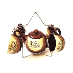 May include: A brown ceramic tea set with a teapot and four cups. The set features a mushroom design and the words "P.P.P.G. MUSHROOM" on the teapot and cups.