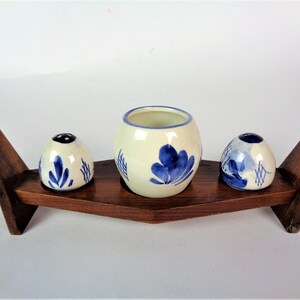 May include: A set of three blue and white ceramic salt and pepper shakers with a floral design, displayed on a wooden stand.
