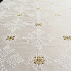 May include: White tablecloth with a delicate floral pattern embroidered in green and white. The tablecloth has a subtle sheen and a soft texture.