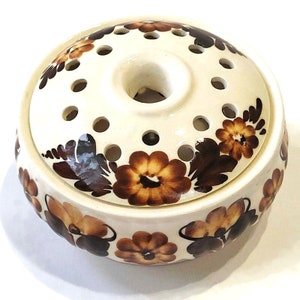 Op de afbeelding: Een witte keramische bloemenvaas met bruine bloemenmotieven. De vaas heeft een ronde basis en een centraal gat met meerdere kleinere gaten rond de rand.