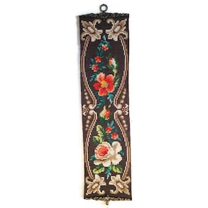 May include: A brown and beige floral tapestry with a metal hanging loop at the top. The tapestry features a repeating pattern of flowers and leaves.
