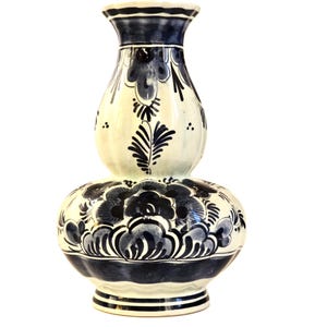May include: A white and blue ceramic vase with a bulbous base and a slender neck. The vase is adorned with intricate floral patterns in shades of blue. The base features a ringed design, and the overall height is approximately 12 inches.