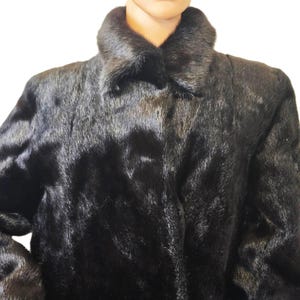 May include: A black fur coat with a classic collar. The coat has a smooth, luxurious texture and appears to be made of high-quality fur. The coat is buttoned up and has long sleeves. The overall style is elegant and timeless.