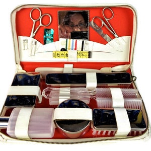 Könnte beinhalten: Weiße Leder-Reise-Kosmetiktasche mit roter Innenausstattung, die ein Set an Pflegeutensilien enthält, darunter einen Kamm, Bürsten, Scheren und ein kleines Fläschchen Kölnisch Wasser.