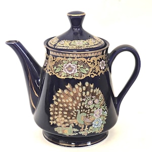 May include: A cobalt blue teapot with a gold trim and a peacock design. The teapot has a lid and a handle.