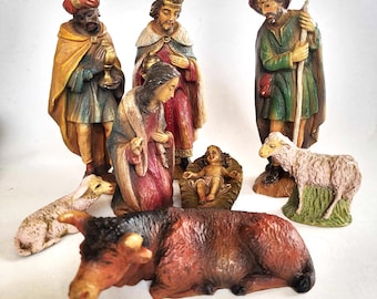 May include: A nativity scene figurine set with a brown ox, a white lamb, a baby Jesus, three wise men, and Mary and Joseph. The figures are made of painted ceramic and have a vintage look.