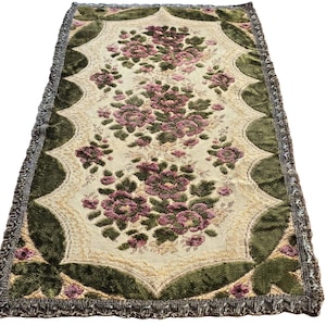 Puede incluir: Una alfombra vintage de tapicería floral con fondo verde y crema. La alfombra presenta un patrón repetitivo de flores rosas y verdes. La alfombra tiene un borde con flecos.
