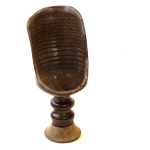 May include: A brown ceramic bowl with a unique, wavy design sits on a pedestal base. The bowl has a textured, speckled finish and a wide, open rim.