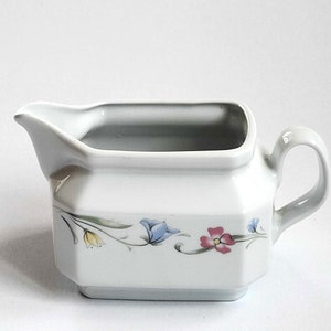 May include: White porcelain gravy boat with a floral design featuring blue, yellow, pink, and green flowers. The boat has a handle on the right side.