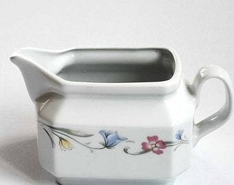 May include: White porcelain gravy boat with a floral design featuring blue, yellow, pink, and green flowers. The boat has a handle on the right side.