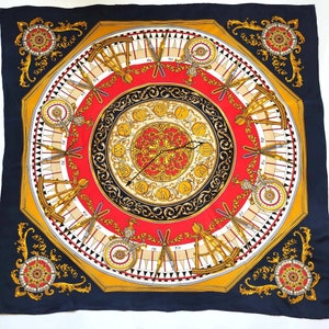 May include: A black silk scarf with a colorful design featuring a clock face, compass, and other intricate details. The design is surrounded by a gold frame and has a red, gold, and black color scheme.