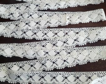 May include: Five pieces of white cotton lace trim with a scalloped edge and a delicate floral pattern.