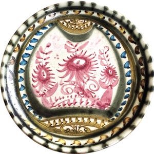May include: A round ceramic plate with a white background and a decorative design in shades of pink, blue, and gold. The design features stylized flowers and leaves.