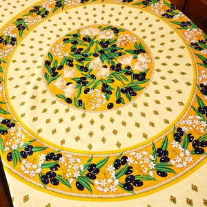 Peut inclure: Une nappe jaune et blanche avec un motif circulaire représentant des olives noires, des feuilles vertes et des gousses d'ail blanches. Le motif est entouré d'une bordure en forme de corde.