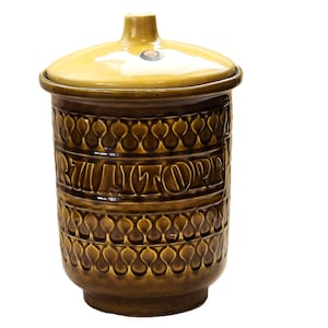 Könnte beinhalten: Eine braune Keramikdose mit Deckel, die ein sich wiederholendes Muster aus tropfenförmigen Formen und das Wort "RUTOPIA" in Prägung aufweist.