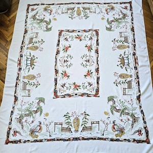 Pode incluir: Uma toalha de mesa retangular branca com um padrão repetitivo de figuras com chapéus cónicos, vasos decorativos, pagodes e árvores estilizadas. O design inclui uma borda retangular central preenchida com motivos florais vermelhos.