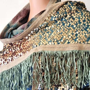 May include: A teal blue, brown, and gold sequined scarf with a green fringe. The scarf has a tan trim.