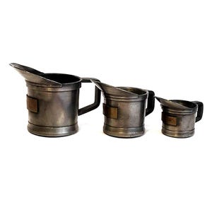 May include: Three vintage pewter oil cans with a spout and a handle. The cans are different sizes and have a copper band around the middle.
