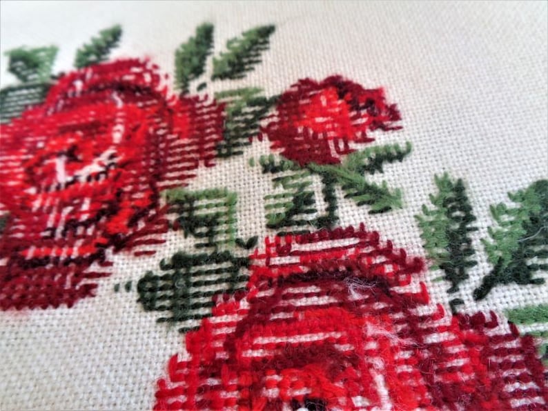 May include: Close-up of a white fabric with red and green embroidered roses. The roses are stitched with a cross-stitch pattern.