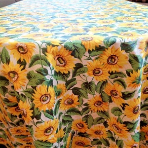 May include: A white tablecloth with a sunflower pattern. The tablecloth is covered in yellow sunflowers with green leaves on a white background.