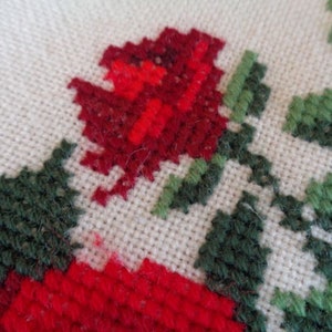 May include: Close-up of a red and green embroidered design on a white fabric. The design features a red rose with green leaves.