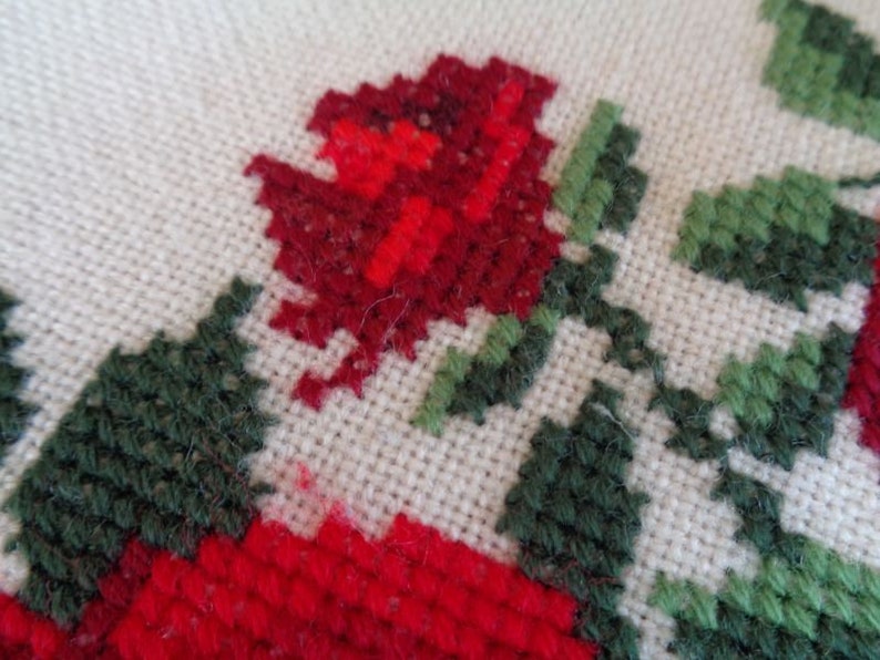 May include: Close-up of a red and green embroidered design on a white fabric. The design features a red rose with green leaves.