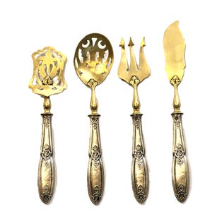 May include: Set of four antique silver-plated serving utensils with ornate handles. The utensils include a serving spoon, a cake server, a fork, and a butter knife.