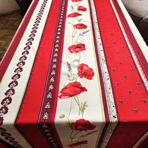 Puede incluir: Un mantel rojo y crema con un diseño floral. El mantel presenta rayas verticales con patrones alternos, que incluyen amapolas rojas, lavanda y bordes decorativos. El diseño general es de un estilo clásico y elegante.