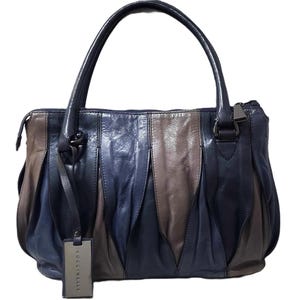 May include: A dark blue and brown leather handbag with a pleated design. The bag has two top handles and a zipper closure. The brand name "Coccinelle" is visible on a tag attached to the bag.