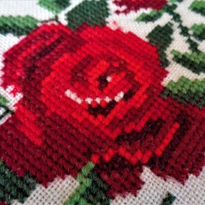 May include: Close-up of a red embroidered rose with green leaves on a white fabric background.