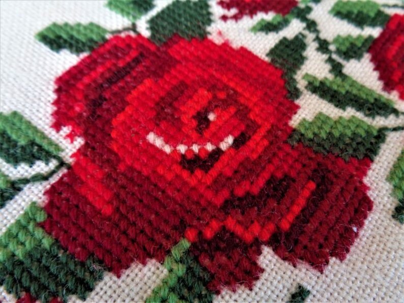 May include: Close-up of a red embroidered rose with green leaves on a white fabric background.