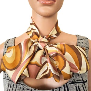 May include: A patterned silk scarf in shades of brown, beige, and pink. The scarf is knotted at the neck, displaying a retro design of curved lines. The scarf's colours and pattern are prominent, creating a striking visual effect.