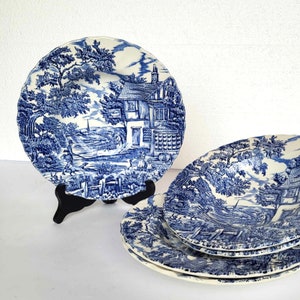 May include: A set of four blue and white ceramic plates with a cottage and countryside scene. The plates feature a blue and white floral pattern.