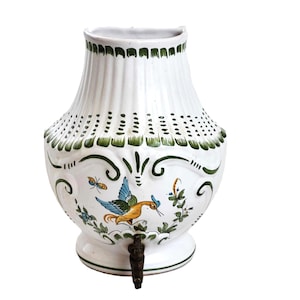 May include: White ceramic pitcher with a green and floral design. A bird with blue and yellow accents is painted on the front. The pitcher has a spout and a handle.