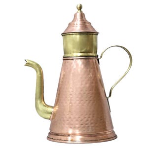 Op de afbeelding: Een koperen en messing kan met een gehamerde textuur. De kan heeft een lange, gebogen tuit en een handvat. De bovenkant van de kan is van messing en heeft een decoratieve knop. De body van de kan is van koper.