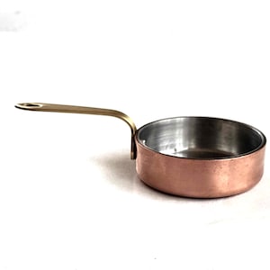Op de afbeelding: Een kleine koperen pan met een messing handvat. De pan heeft een roestvrijstalen binnenkant.