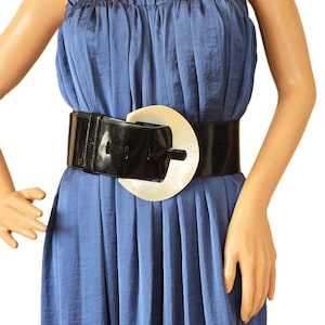 May include: A wide black patent leather belt with a large, off-white, oval-shaped buckle.