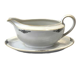 May include: White porcelain gravy boat with a gold rim and black floral design. The boat is on a matching saucer.
