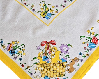May include: White tablecloth with a yellow border featuring a basket of Easter bunnies and colorful eggs. The basket is filled with colorful eggs and surrounded by flowers.