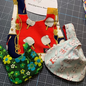 May include: Three fabric scraps for a sewing project. One is red with a white and blue pattern of tennis rackets and balls. Another is green with a blue and white floral pattern. The third is blue with a white bunny rabbit pattern. The text "Girly Girl Style" and "Mini Japanese Knot" is visible on the red fabric.