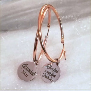 May include: Rose gold hoop earrings with a dangling charm. The charm on the left says "Jeremiah 29:11" and the charm on the right says "The Lord is my Rock Psalm 18:2".