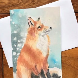 Carte de Noël de renard de neige regardant par l’artiste britannique