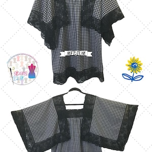 Può includere: Blusa a quadri bianchi e neri con bordino in pizzo nero. La blusa ha una scollatura quadrata e maniche corte. La blusa è appesa a un appendiabiti e l'etichetta dice "MEDIUM".