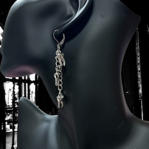 May include: Silver dangle earrings with a chain and multiple tooth charms.